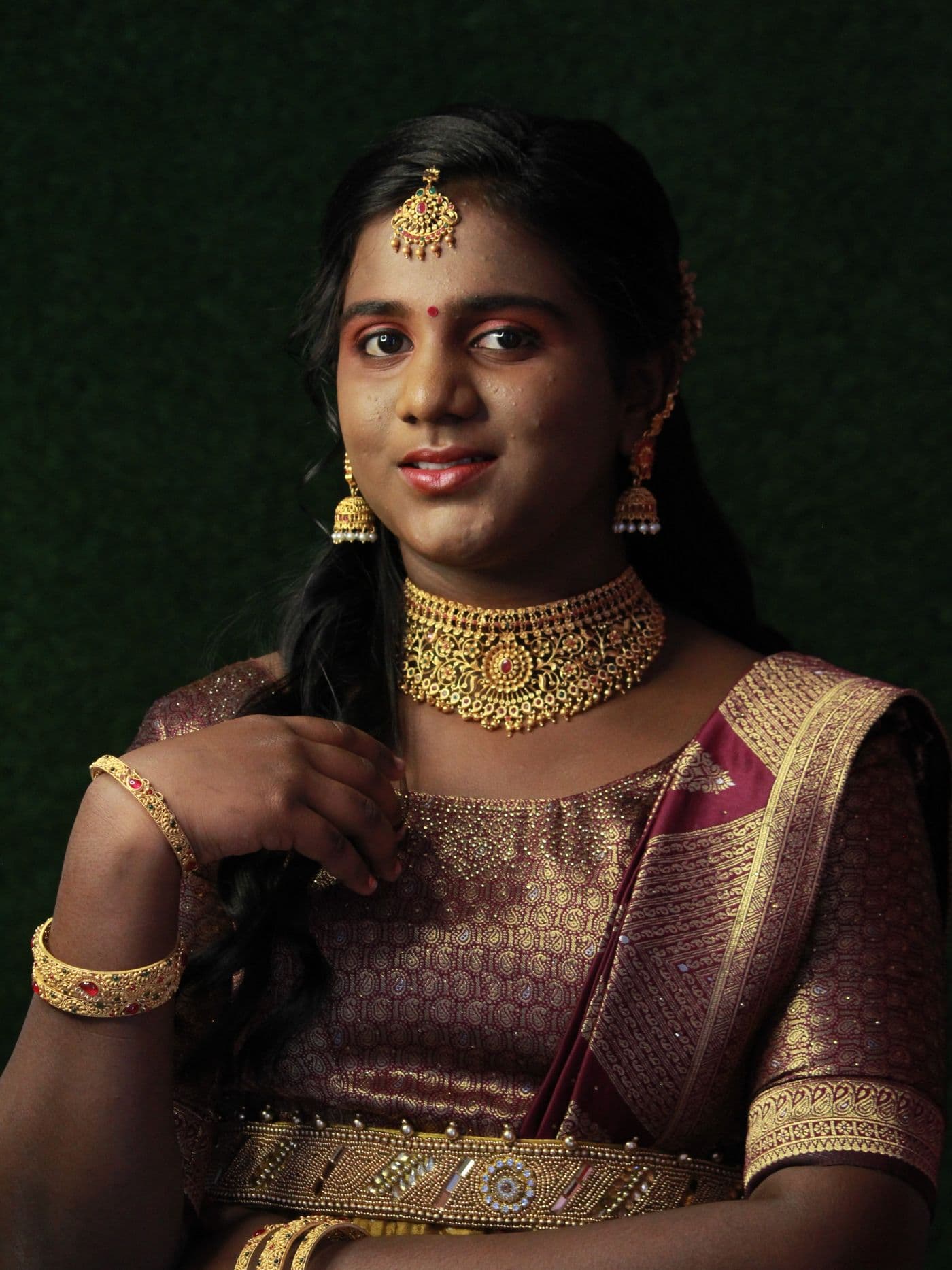 Woman in a deep green and gold saree against a dark backdrop