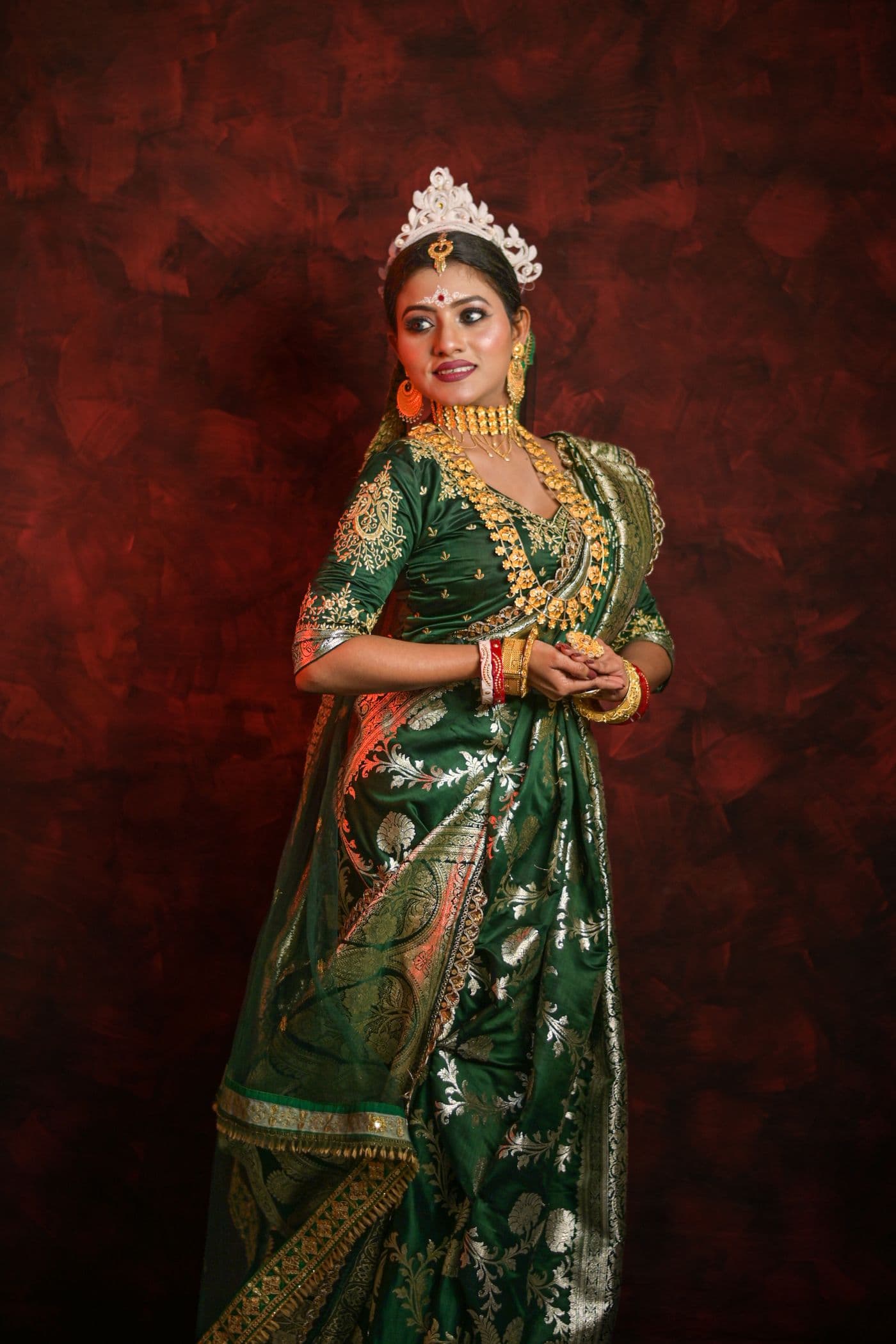 Woman in a green and red saree against a rich red backdrop