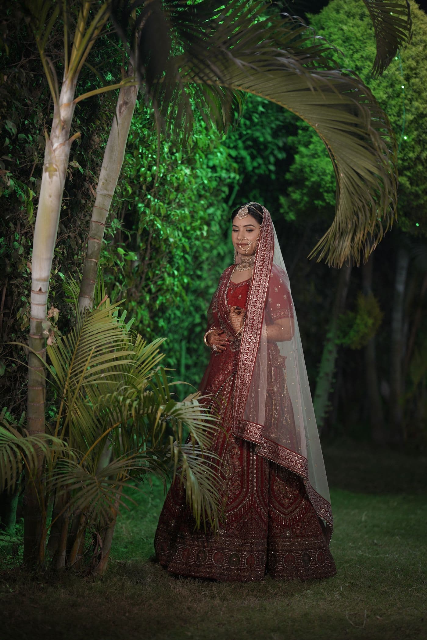 Bride in a deep red lehenga in a garden at night