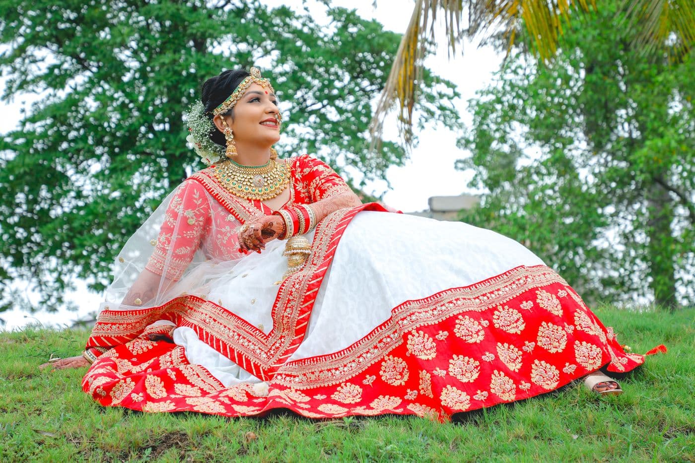 Bride in a red and white lehenga seated on a lawn