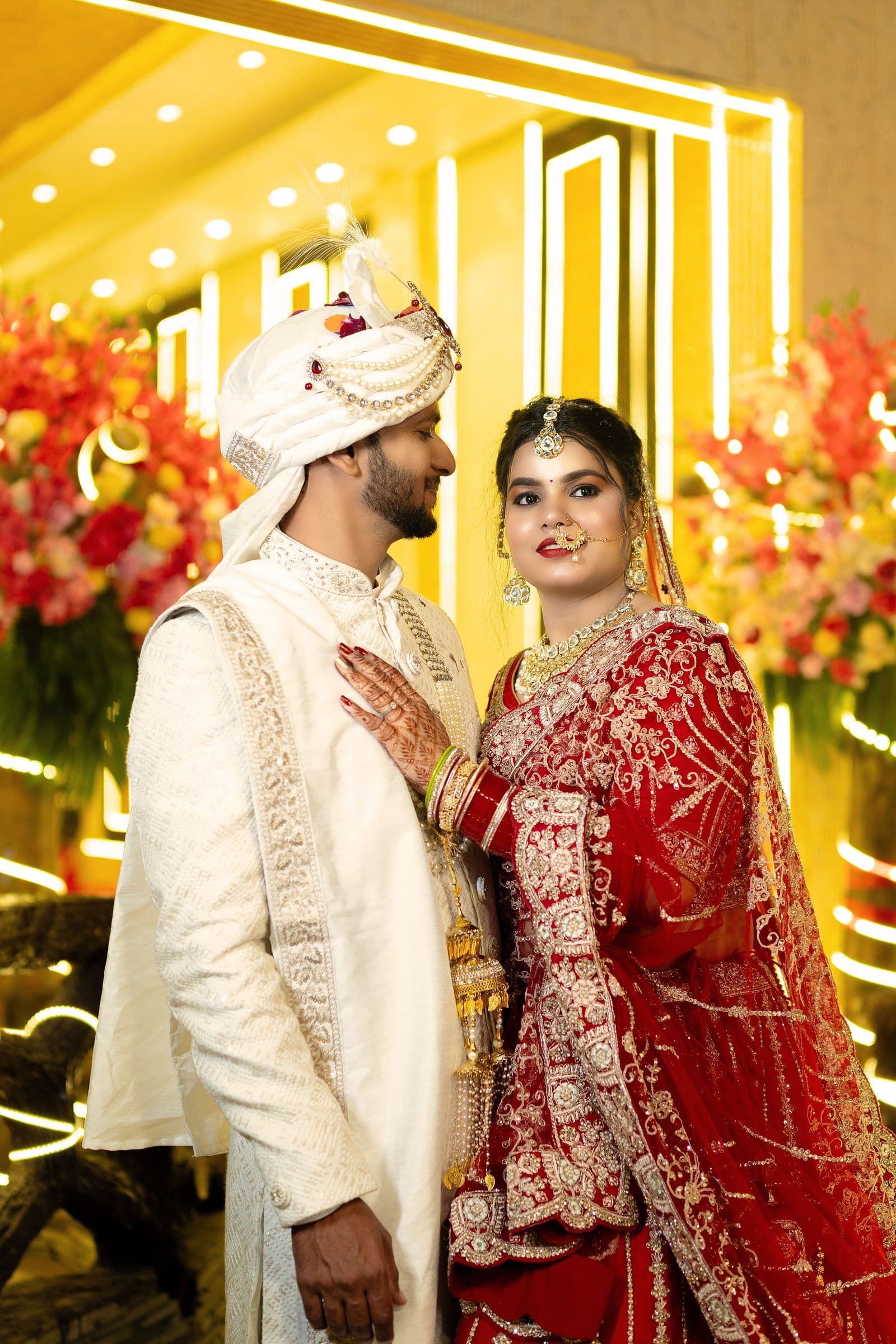 Bride in a red lehenga beside the groom in a white sherwani