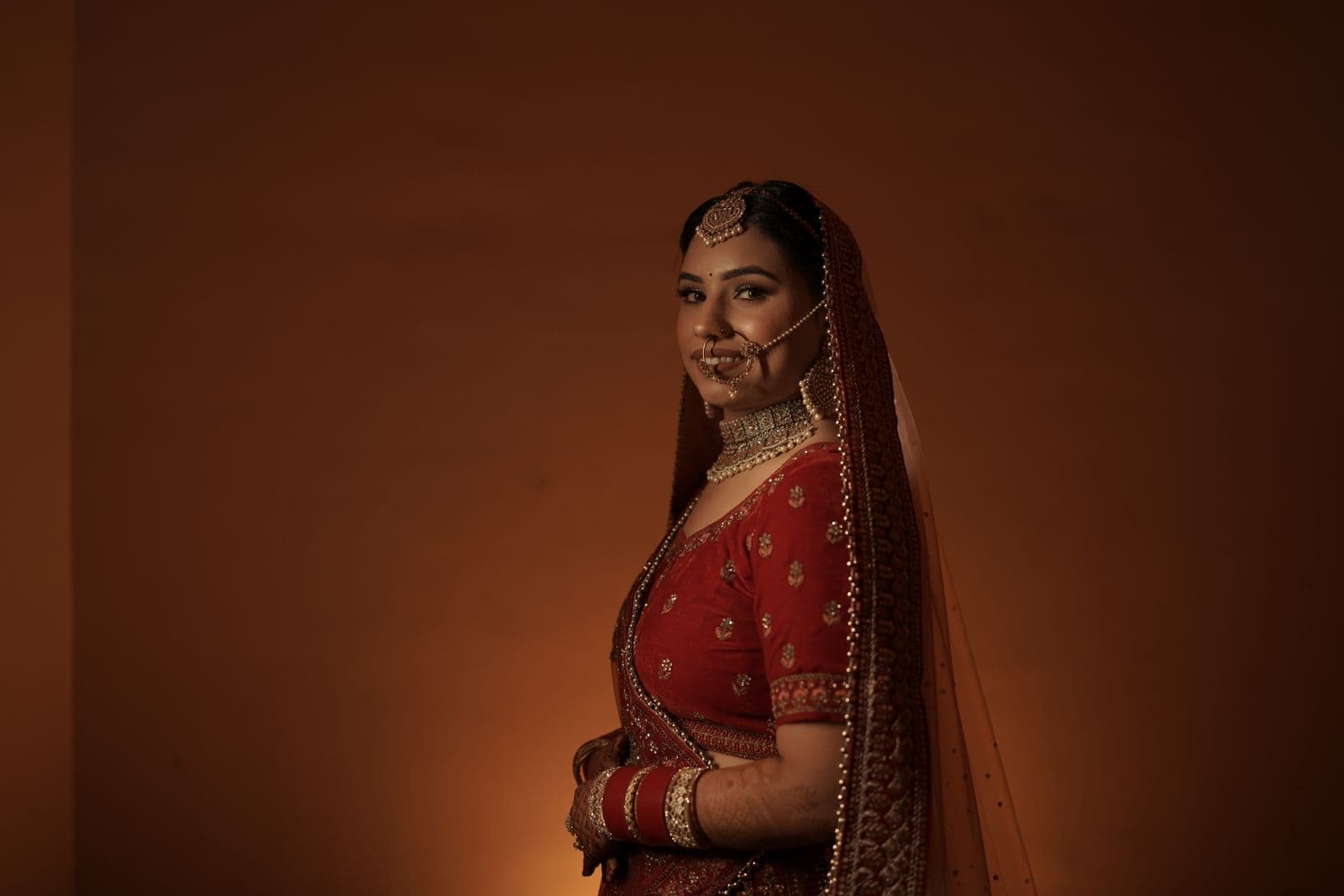 Bride in a richly embellished lehenga against a warm amber backdrop