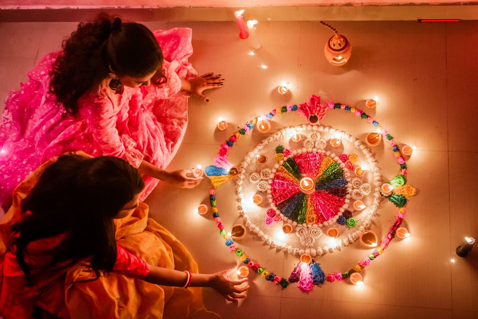 Women in traditional attire arranging a Diwali rangoli by candlelight
