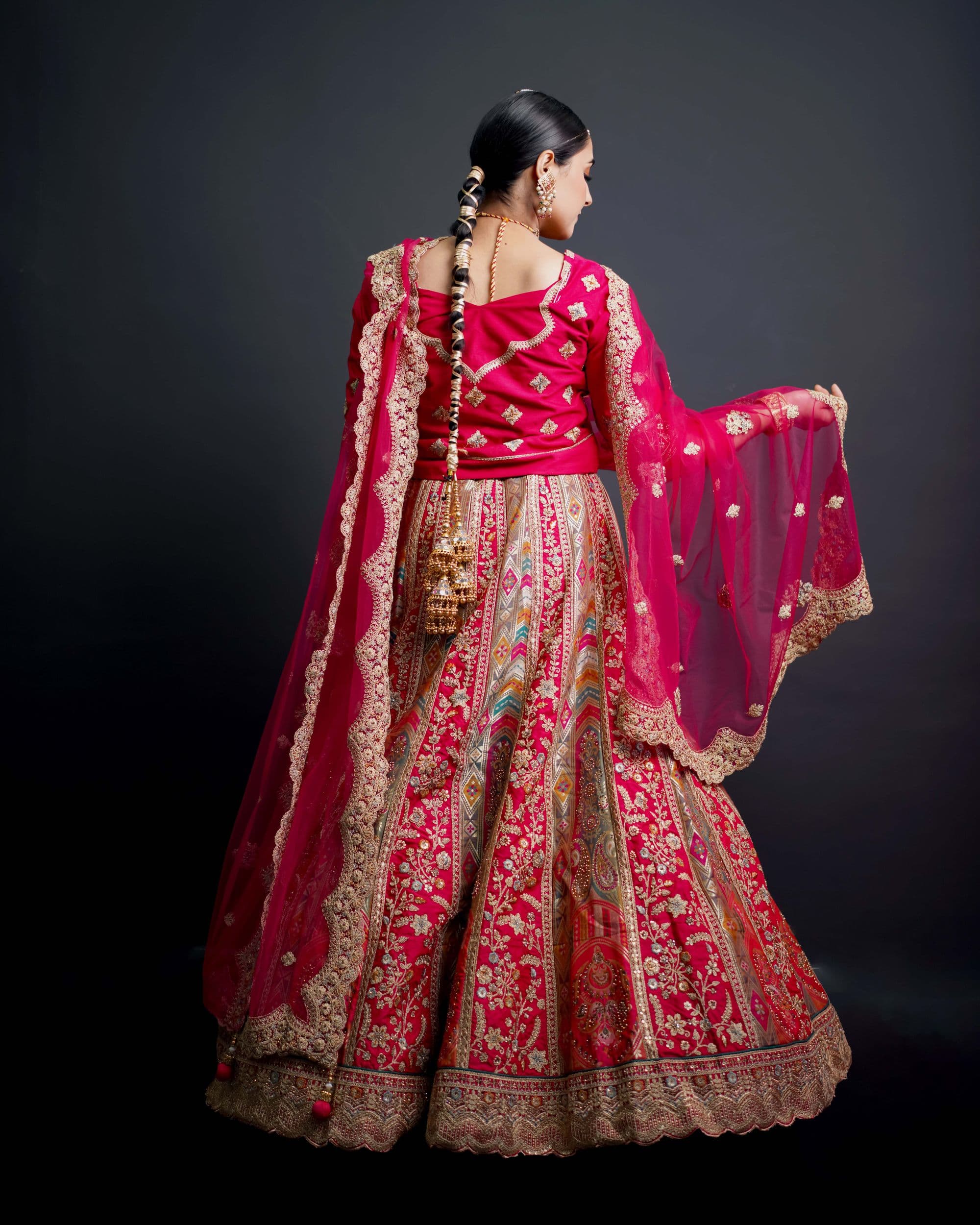 Bride in an embellished red lehenga photographed from behind against a dark backdrop