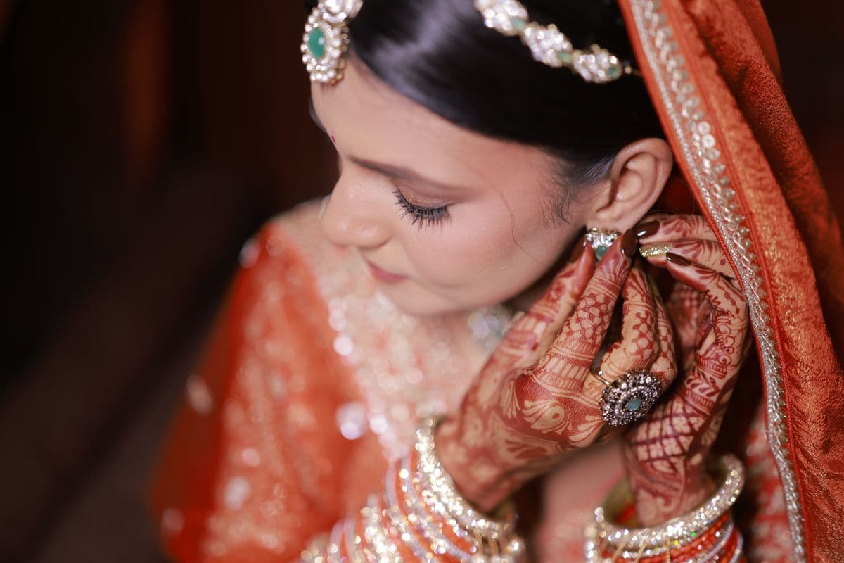 Bride adjusting her earrings, showcasing henna and jewellery