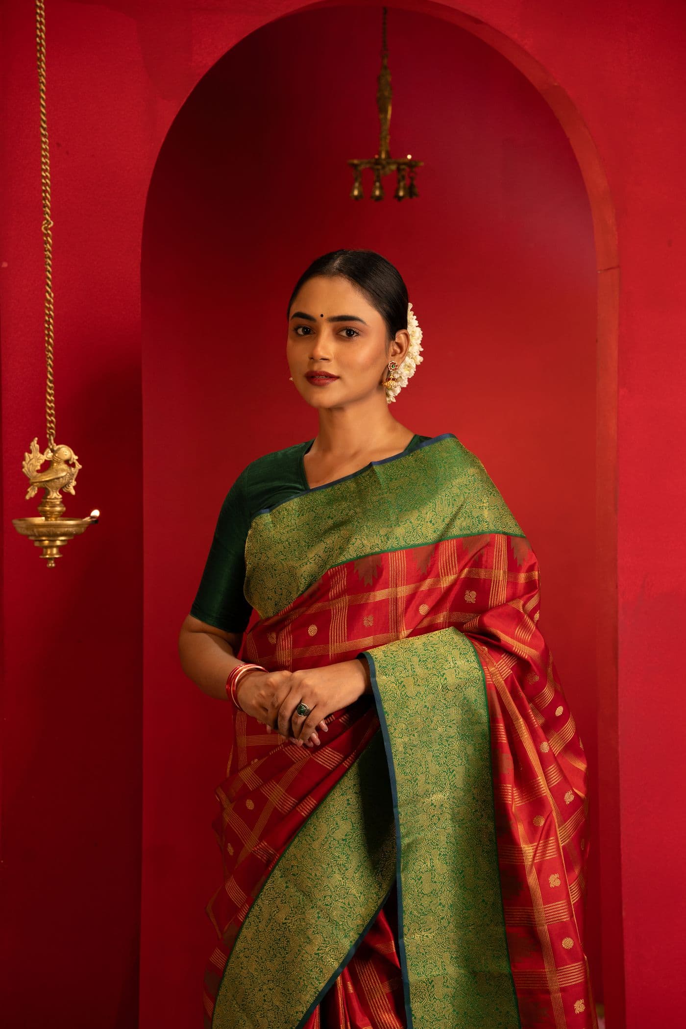 Woman in a green and gold saree standing within a red archway